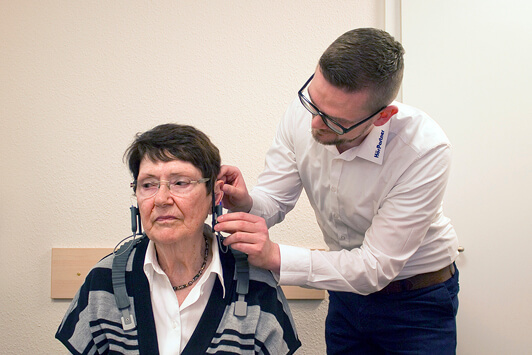 Hörtest bei Seniorin: Hörakustiker passt Kopfhörer zur Hörgeräteanpassung an.