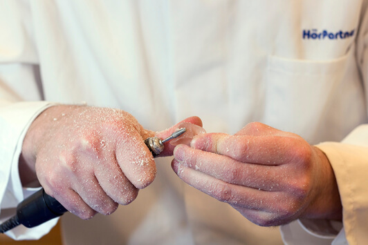 Ein Hörakustiker schleift ein Hörgerät individuell für die optimale Hörgeräteanpassung.